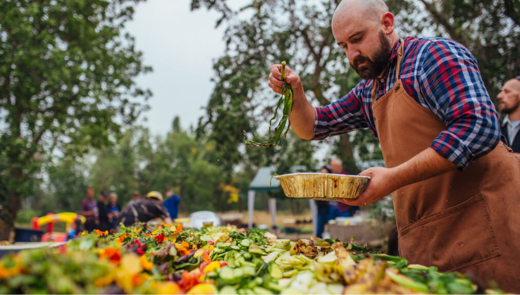 Photo of chef in brown apron tossing table length salad.